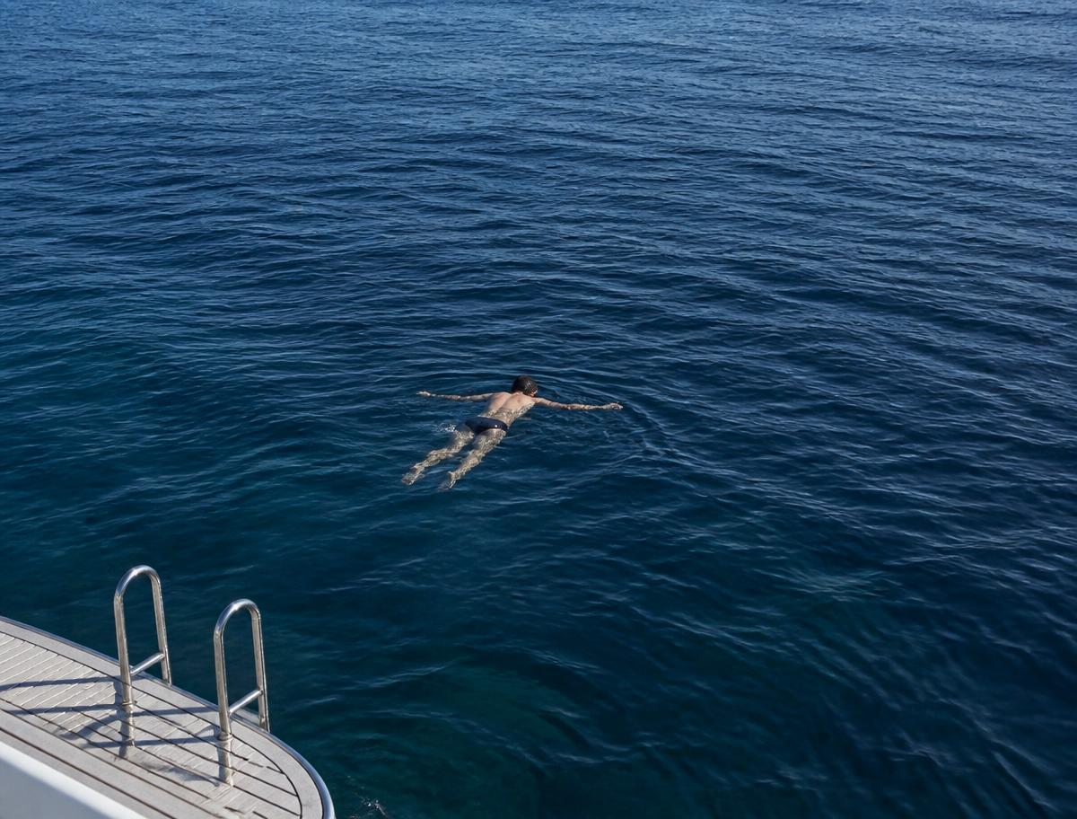A swimmer floating in deep blue Atlantic water beside a boat ladder